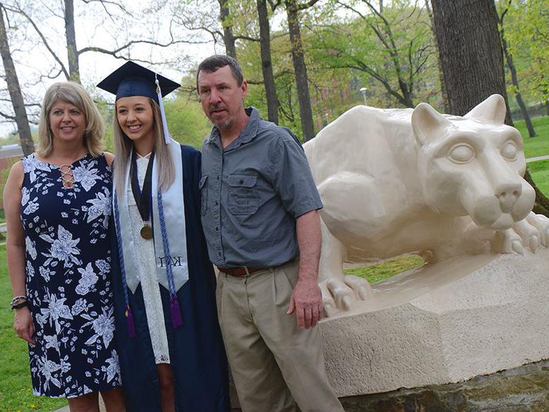 A recent graduate poses with her parents in front of the Lion Shrine at Penn State Altoona